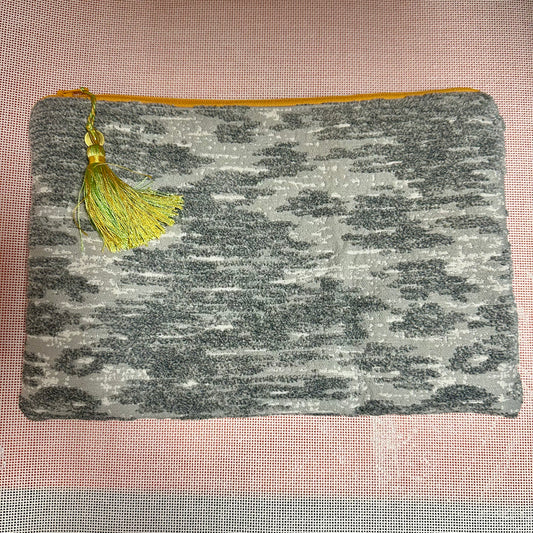 Gray textured pouch with a yellow tassel on a pink textured background