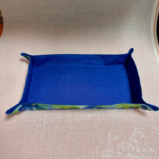 Blue fabric tray with green trim on a beige surface
